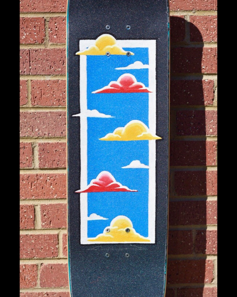 a skateboard with painted griptape depicting red, yellow, and white clouds against a blue background with a white border