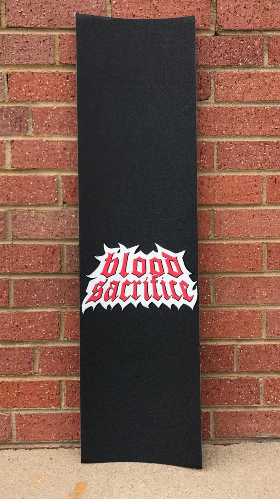 A griptape painting on a skateboard, depicting the words "blood sacrifice" in a red gothic font with thick white outlines